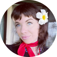 Headshot of a smiling client with a white flower in her hair and a red scarf